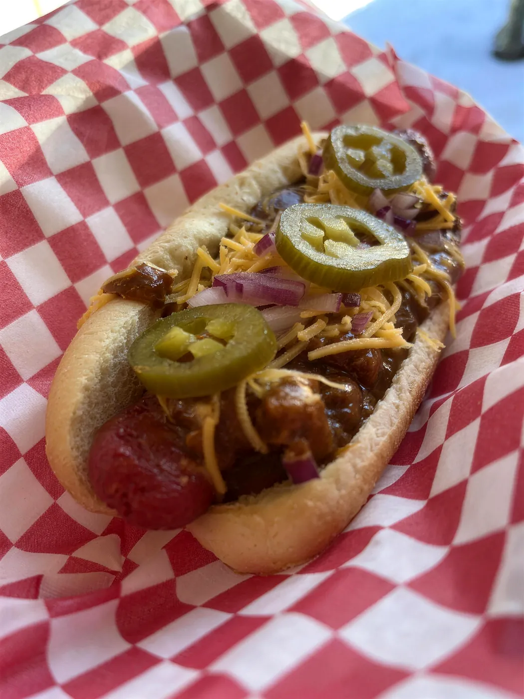 A chili dog with cheddar and jalapeños on checkered paper