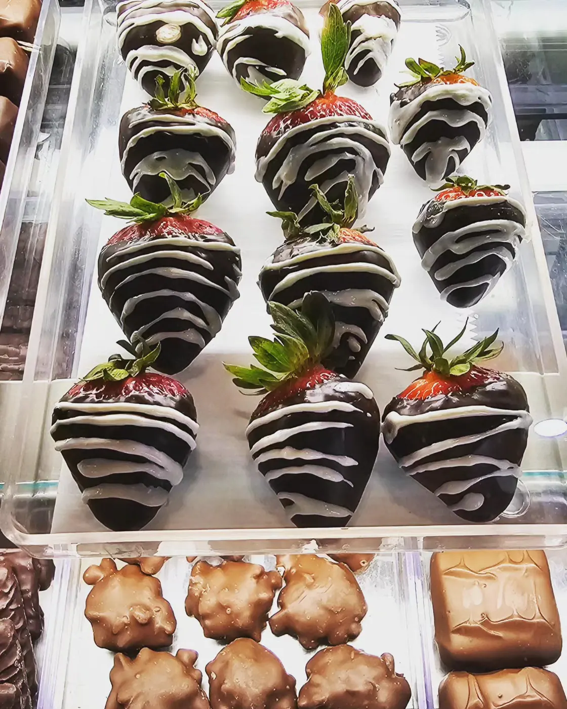 Chocolate-dipped strawberries with white chocolate stripes in the display case